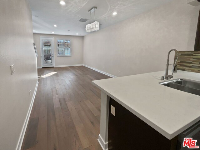 kitchen with dark hardwood / wood-style floors, hanging light fixtures, a notable chandelier, a kitchen island, and sink