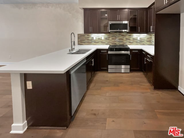 kitchen featuring sink, light wood-type flooring, decorative backsplash, dark brown cabinetry, and appliances with stainless steel finishes