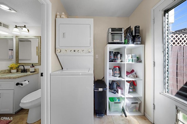 laundry area featuring stacked washer / dryer, sink, a textured ceiling, and light tile patterned floors