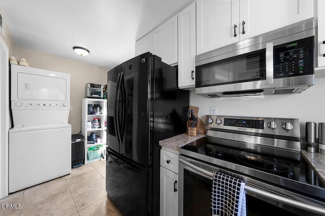 kitchen with light tile patterned floors, light stone counters, white cabinets, stacked washer and clothes dryer, and appliances with stainless steel finishes