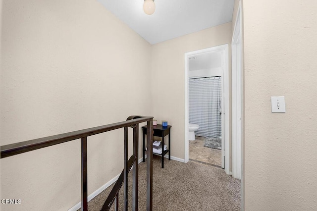 hallway with an upstairs landing, baseboards, and carpet