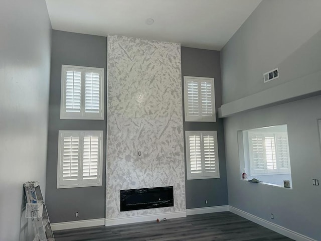 unfurnished living room with dark hardwood / wood-style flooring, a fireplace, a wealth of natural light, and a high ceiling