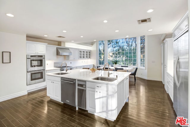 kitchen featuring sink, stainless steel appliances, white cabinets, wall chimney exhaust hood, and an island with sink