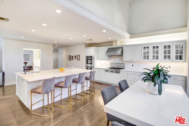 kitchen with white cabinets, a kitchen breakfast bar, wall chimney range hood, and a kitchen island with sink