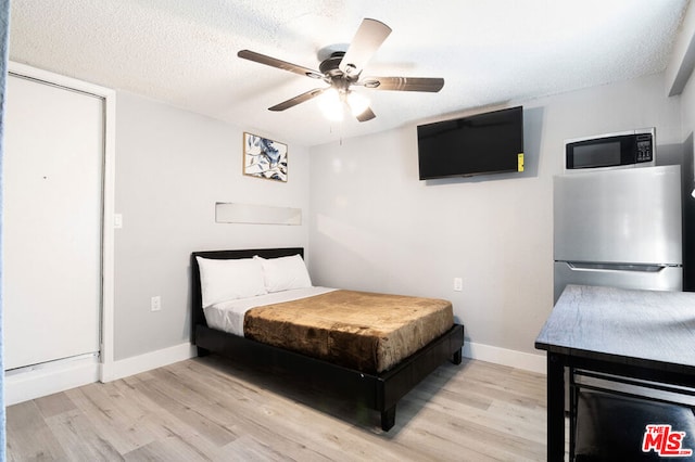 bedroom featuring stainless steel fridge, light wood-type flooring, a textured ceiling, and ceiling fan