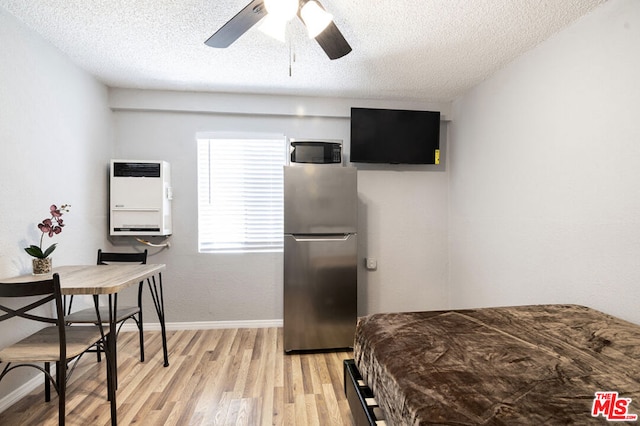 bedroom with stainless steel refrigerator, ceiling fan, heating unit, light hardwood / wood-style floors, and a textured ceiling