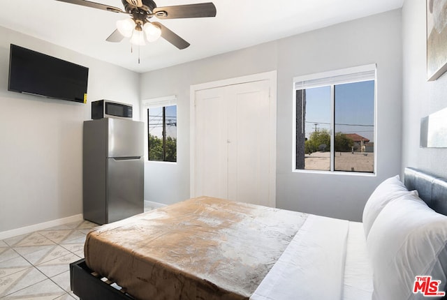 tiled bedroom featuring ceiling fan, stainless steel refrigerator, and a closet