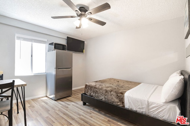 bedroom with ceiling fan, light hardwood / wood-style floors, a textured ceiling, and stainless steel refrigerator