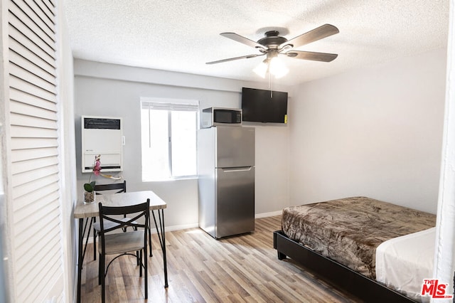 bedroom with light hardwood / wood-style flooring, ceiling fan, a textured ceiling, stainless steel refrigerator, and heating unit