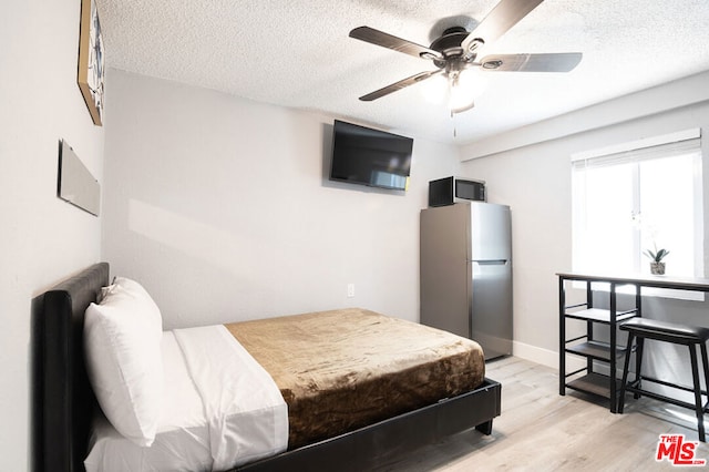 bedroom with ceiling fan, stainless steel fridge, light wood-type flooring, and a textured ceiling