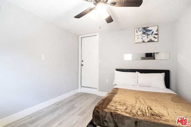 bedroom with a textured ceiling, light hardwood / wood-style flooring, and ceiling fan