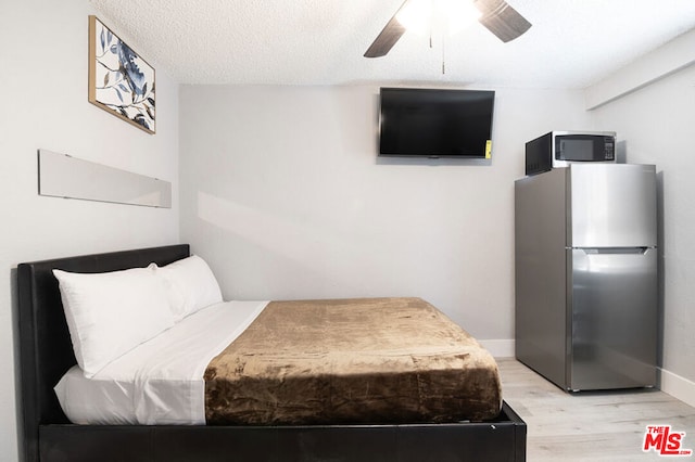 bedroom featuring ceiling fan, stainless steel fridge, light wood-type flooring, and a textured ceiling