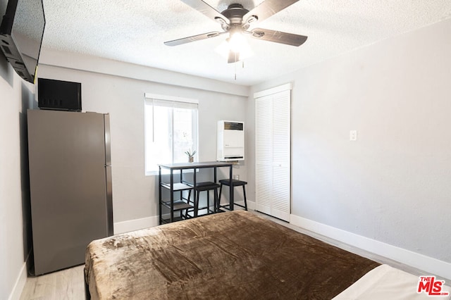 bedroom with ceiling fan, stainless steel fridge, a textured ceiling, light hardwood / wood-style floors, and a closet