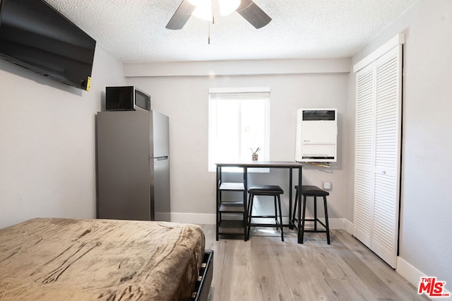 bedroom featuring heating unit, light hardwood / wood-style flooring, ceiling fan, stainless steel fridge, and a closet