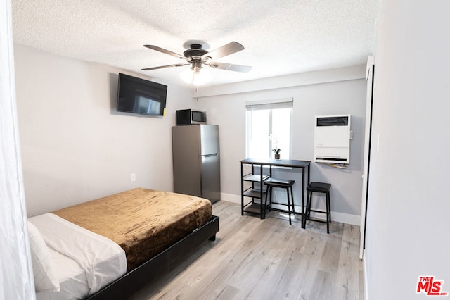 bedroom with stainless steel fridge, light wood-type flooring, a textured ceiling, heating unit, and ceiling fan