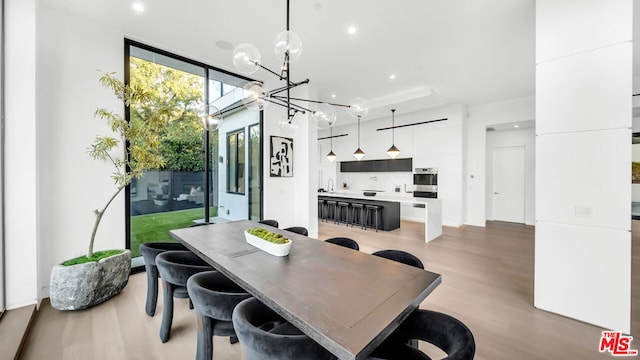 dining room with light wood-type flooring, an inviting chandelier, a wall of windows, and sink