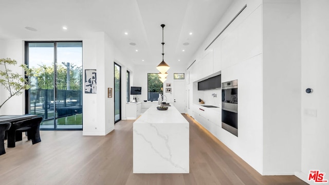 kitchen featuring white cabinetry, a wall of windows, hanging light fixtures, light stone countertops, and light hardwood / wood-style flooring