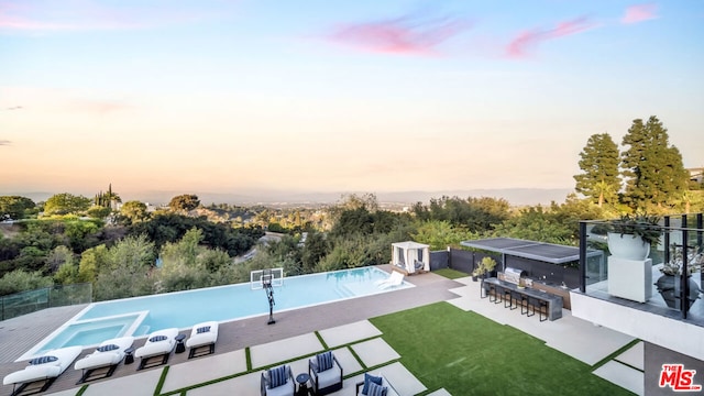 pool at dusk featuring a lawn, a bar, and a patio