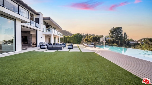 pool at dusk featuring a patio area, a lawn, and an outdoor hangout area