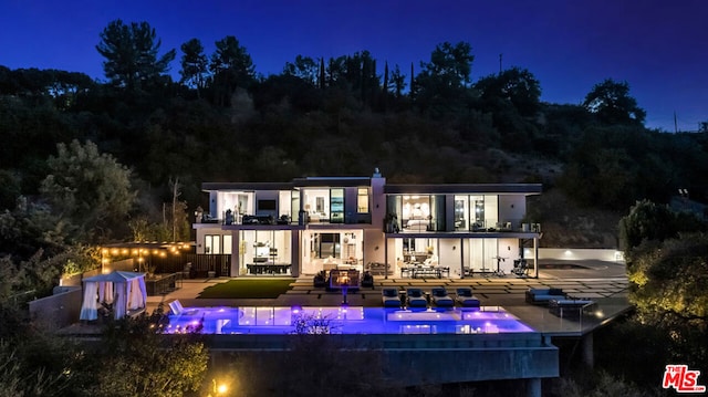 back house at twilight with a patio area and a balcony