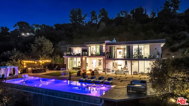 back house at night featuring a balcony, a patio area, and an outdoor hangout area