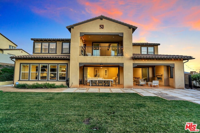 back house at dusk with a yard, a patio area, an outdoor living space, and a balcony