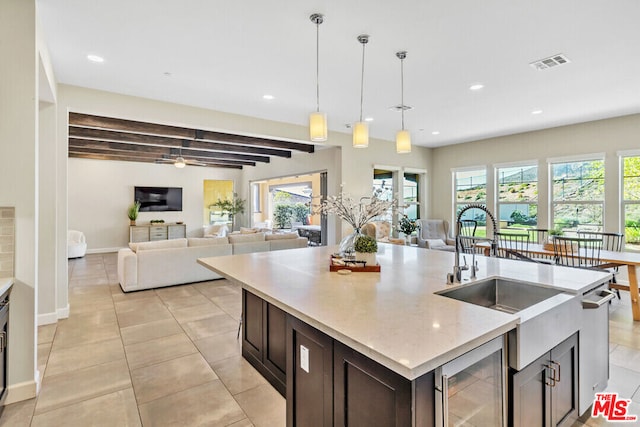 kitchen with beam ceiling, light stone countertops, wine cooler, an island with sink, and decorative light fixtures