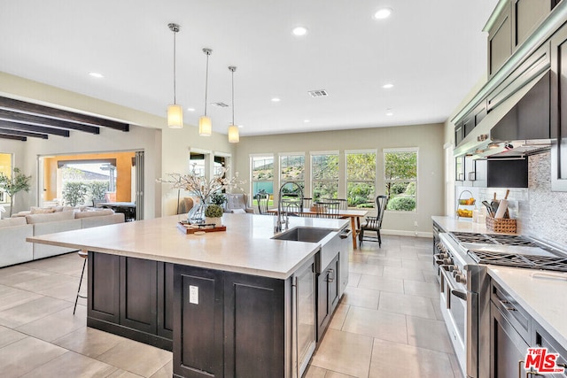 kitchen featuring high end stainless steel range oven, a kitchen island with sink, sink, pendant lighting, and beam ceiling