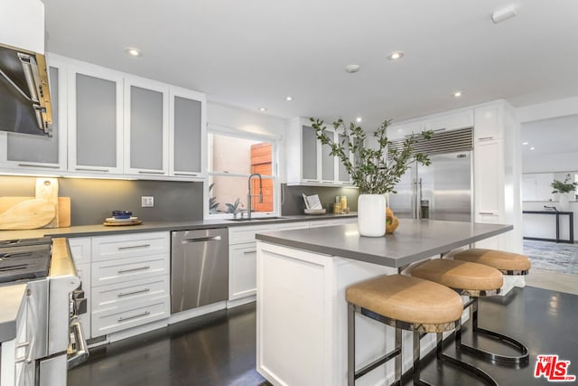 kitchen with high end appliances, sink, a kitchen island, white cabinetry, and a breakfast bar area