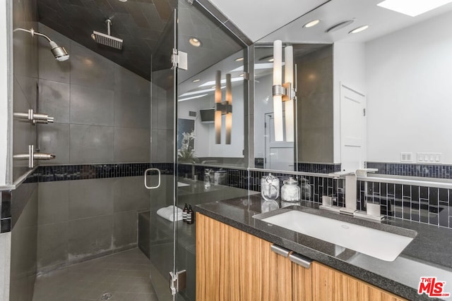 bathroom featuring vanity, a skylight, a shower with door, and tile walls