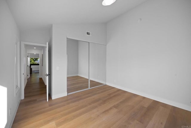 unfurnished bedroom with lofted ceiling, light wood-type flooring, and a closet