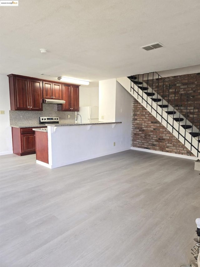 kitchen with brick wall, kitchen peninsula, decorative backsplash, stainless steel range with electric cooktop, and light wood-type flooring