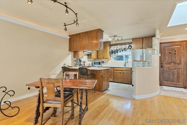 kitchen with kitchen peninsula, a skylight, ornamental molding, and light wood-type flooring