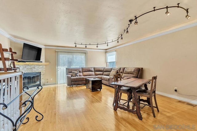 living room featuring hardwood / wood-style flooring, a stone fireplace, and crown molding