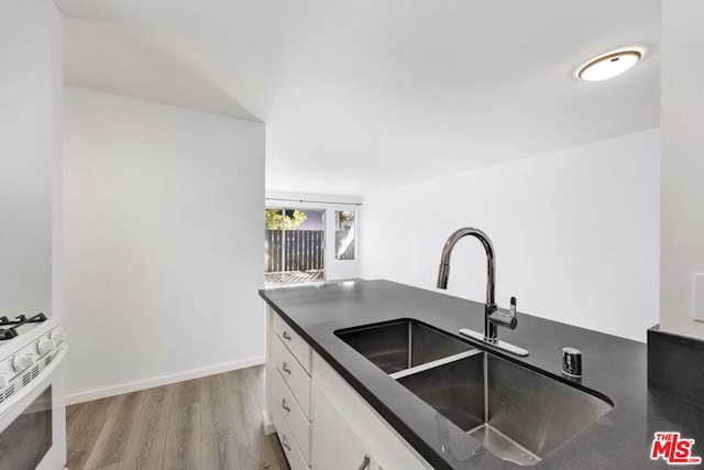 kitchen with light wood-type flooring, white cabinetry, gas range gas stove, and sink