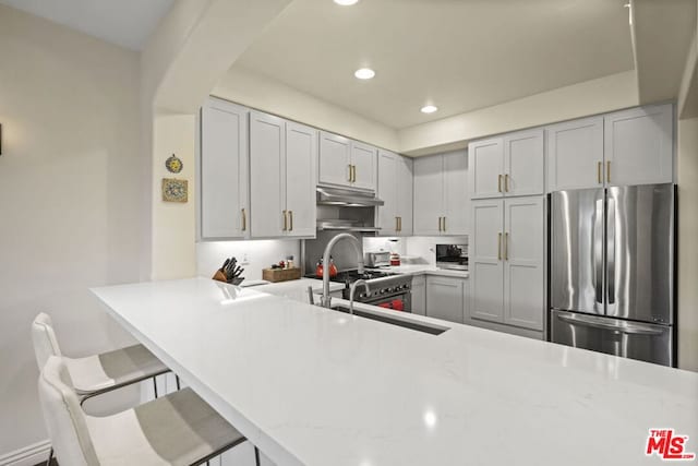 kitchen featuring light stone countertops, stainless steel appliances, gray cabinets, kitchen peninsula, and a breakfast bar area