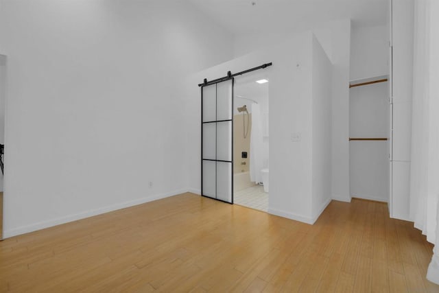 unfurnished bedroom featuring lofted ceiling, ensuite bathroom, a barn door, and light wood-type flooring