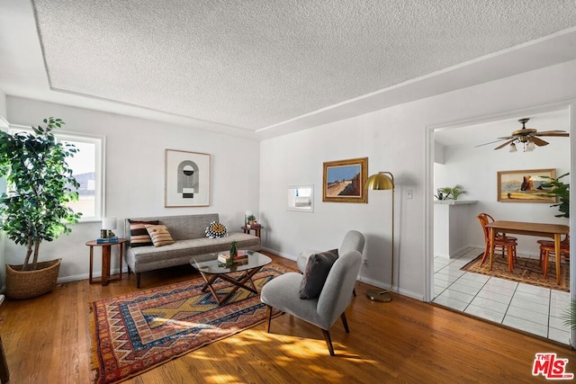 living room featuring ceiling fan, a textured ceiling, and light hardwood / wood-style flooring