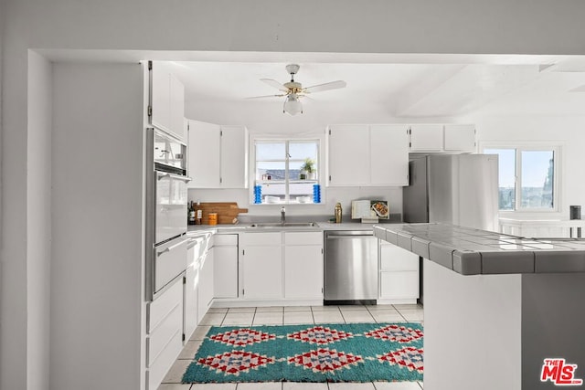 kitchen featuring dishwasher, oven, sink, light tile patterned floors, and white cabinetry