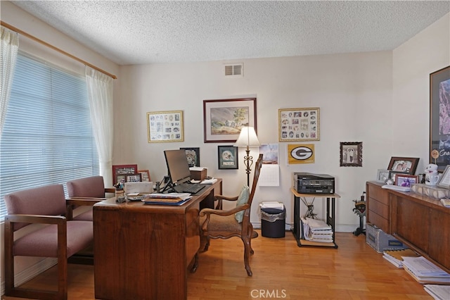 office area with light hardwood / wood-style floors, a textured ceiling, and a wealth of natural light