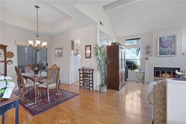 dining area featuring a fireplace, light hardwood / wood-style floors, beamed ceiling, high vaulted ceiling, and a chandelier