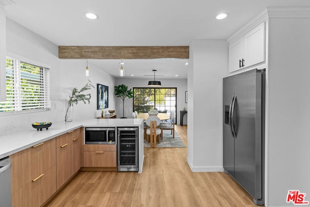 kitchen with pendant lighting, kitchen peninsula, wine cooler, appliances with stainless steel finishes, and white cabinetry