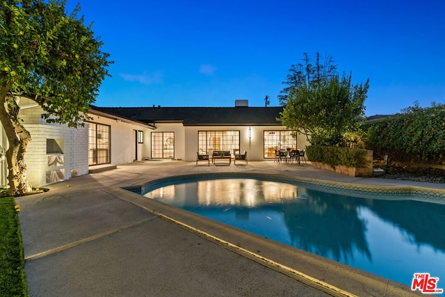 pool at dusk featuring french doors and a patio