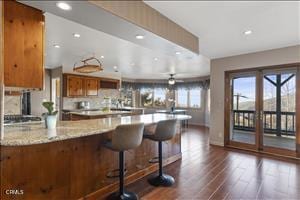 kitchen with a breakfast bar area, kitchen peninsula, light stone countertops, and dark wood-type flooring