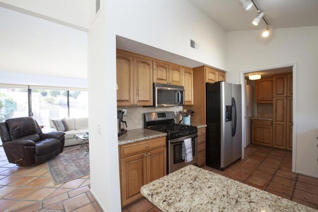 kitchen with decorative backsplash, light stone counters, stainless steel appliances, and a high ceiling