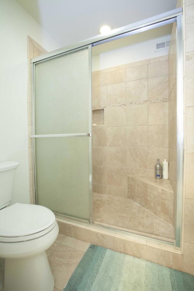 bathroom with tile patterned flooring, toilet, and a shower with door