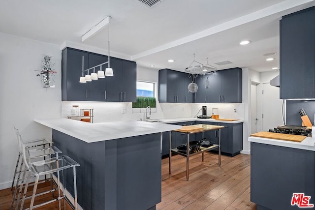 kitchen with a kitchen bar, kitchen peninsula, sink, blue cabinetry, and pendant lighting