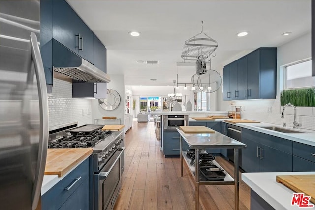 kitchen featuring appliances with stainless steel finishes, dark wood-type flooring, sink, blue cabinetry, and pendant lighting