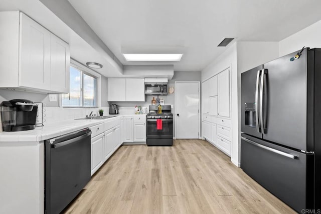 kitchen featuring tile countertops, sink, light wood-type flooring, white cabinetry, and stainless steel appliances