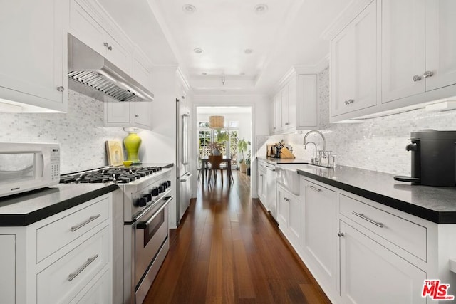 kitchen featuring high quality appliances, sink, wall chimney exhaust hood, dark hardwood / wood-style floors, and white cabinetry